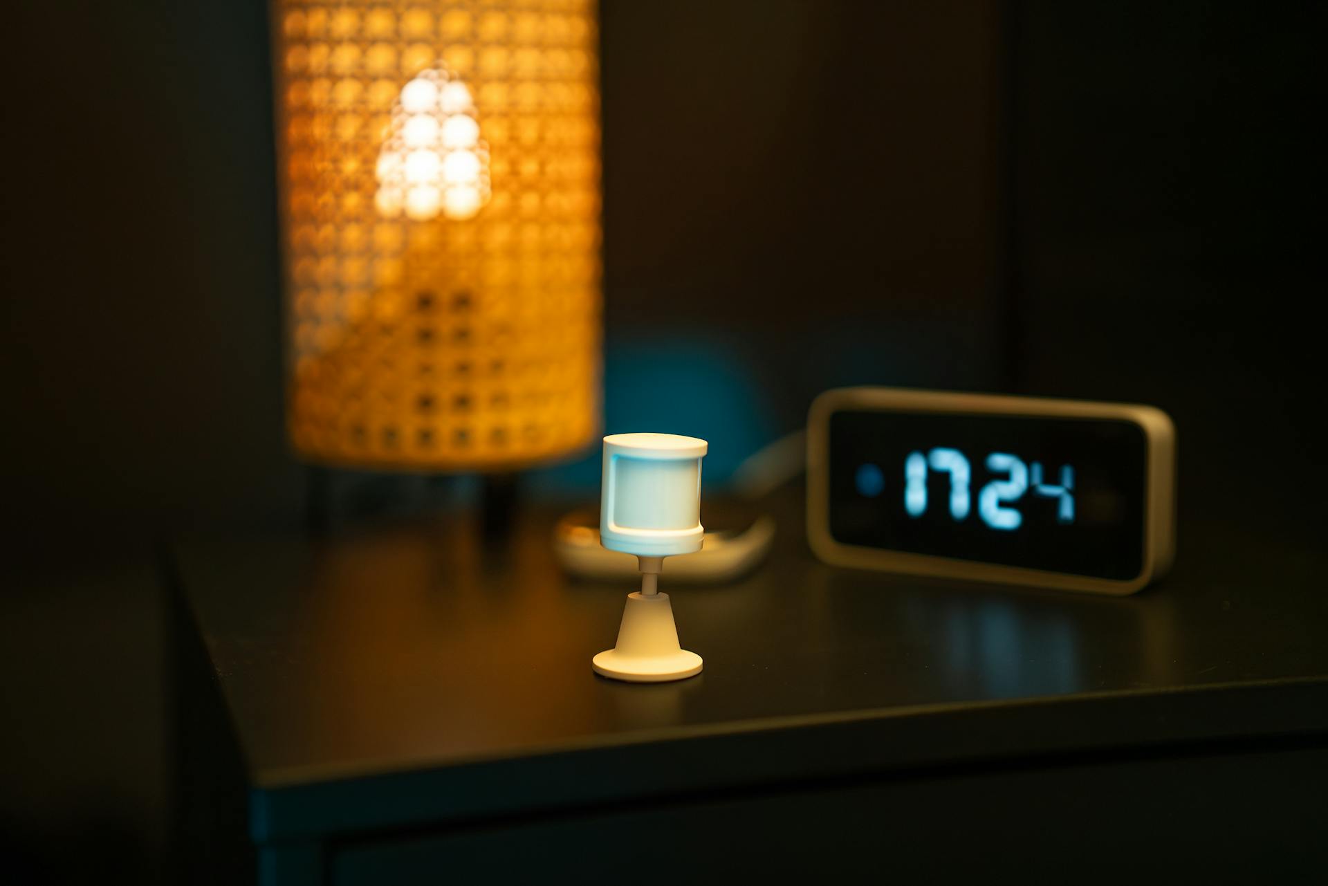 Connected smart home sensor and digital clock glowing on a bedside table at night